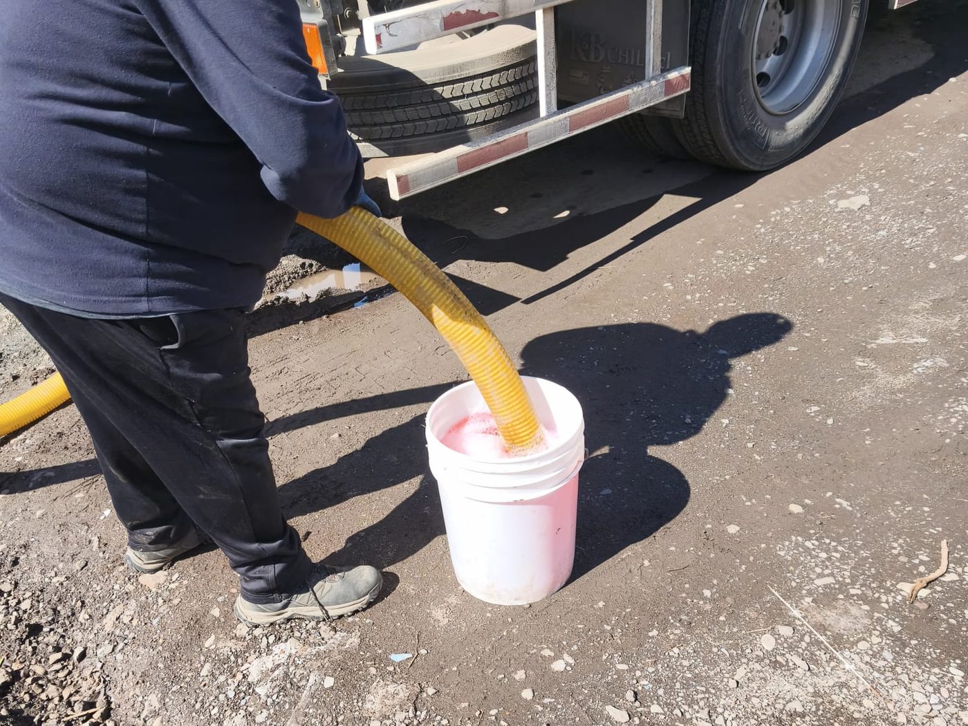 Un operario sostiene la manguera de succión del camión dentro de un balde con el producto.